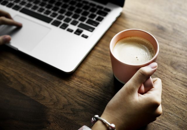 woman holding mug of coffee next to laptop
